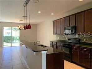 A kitchen features dark wood cabinets, black appliances, a granite island, and tile flooring — 2095 VELVET LEAF DRIVE, OCOEE, FL