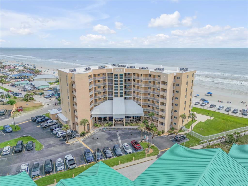 An aerial view shows a multi-story beachfront condominium building with a parking lot — 421 S ATLANTIC AVENUE UNIT 509, NEW SMYRNA BEACH, FL