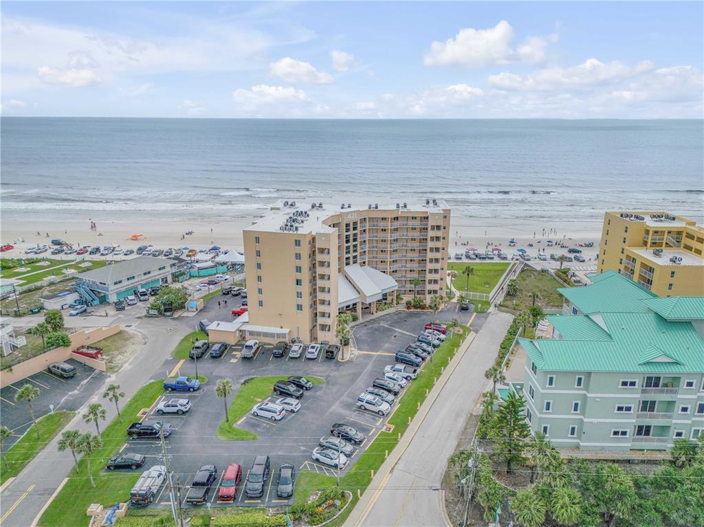 An aerial view shows a multi-story tan hotel building near a beach and parking lot — 421 S ATLANTIC AVENUE UNIT 509, NEW SMYRNA BEACH, FL
