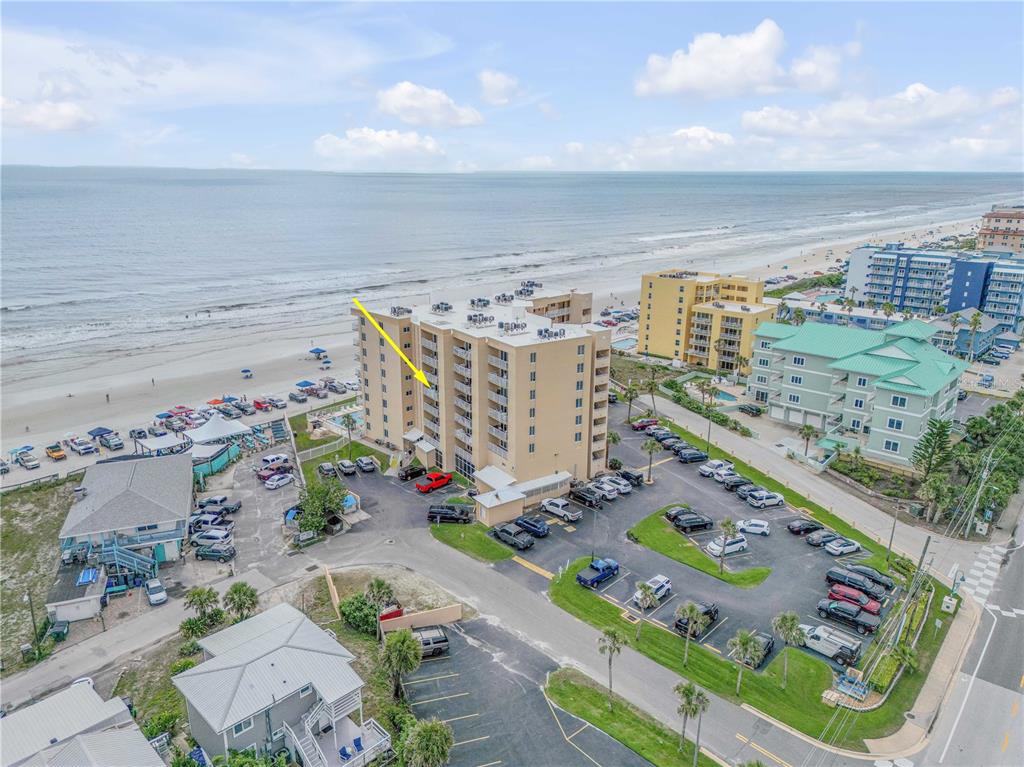 An aerial view shows a multi-story beachfront condominium building with a parking lot and ocean — 421 S ATLANTIC AVENUE UNIT 509, NEW SMYRNA BEACH, FL