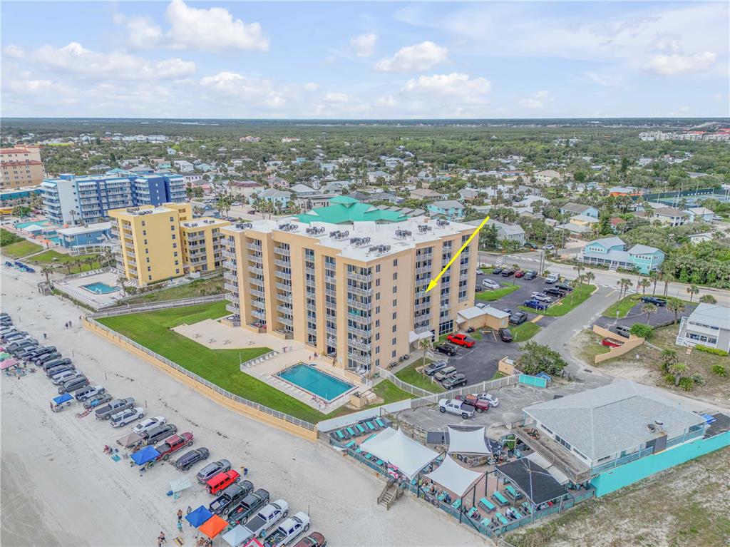 An aerial view shows a multi-story tan beachfront condominium building with a pool and parking — 421 S ATLANTIC AVENUE UNIT 509, NEW SMYRNA BEACH, FL