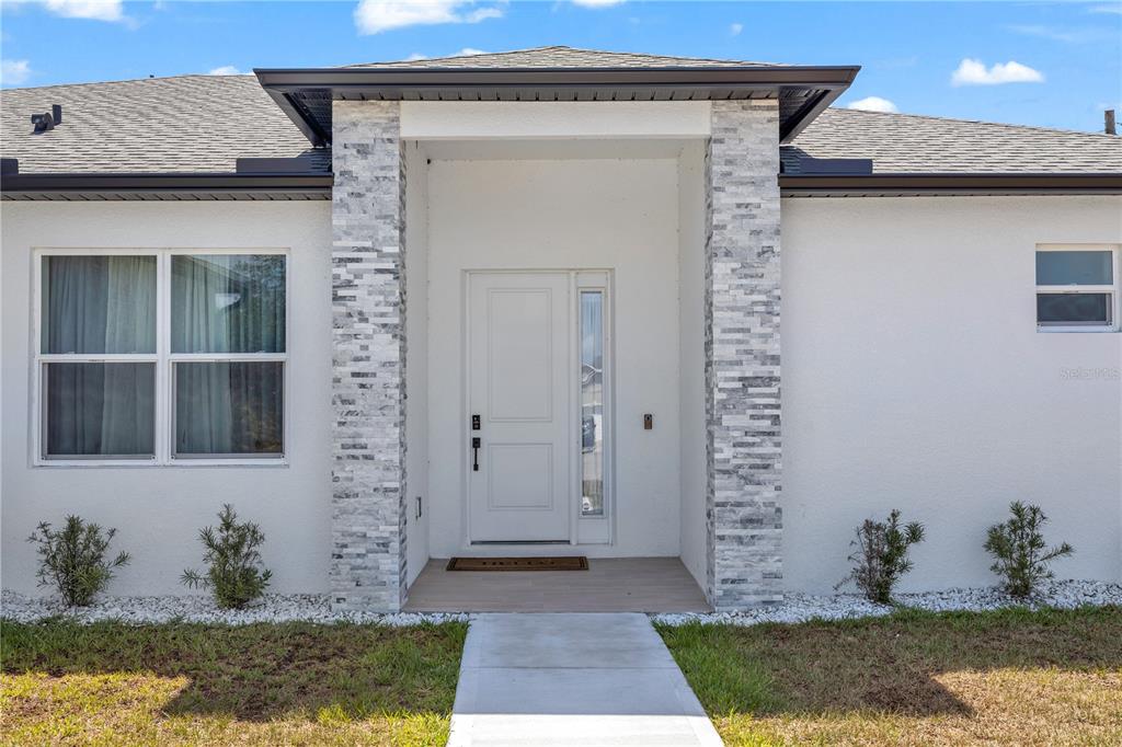 The exterior of a house features a white stucco facade, stone-accented entryway, and a walkway — 780 KANGAROO COURT, DELTONA, FL