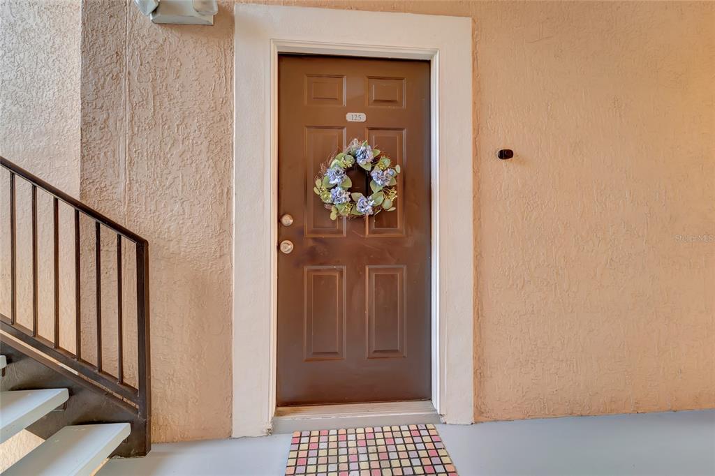 A brown front door with a wreath and unit number 125 sits beside a staircase — 4110 CENTRAL SARASOTA PARKWAY UNIT 125, SARASOTA, FL