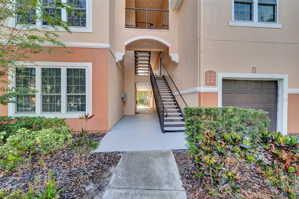 An exterior view of an apartment building entrance featuring a staircase and a garage door — 4110 CENTRAL SARASOTA PARKWAY UNIT 125, SARASOTA, FL