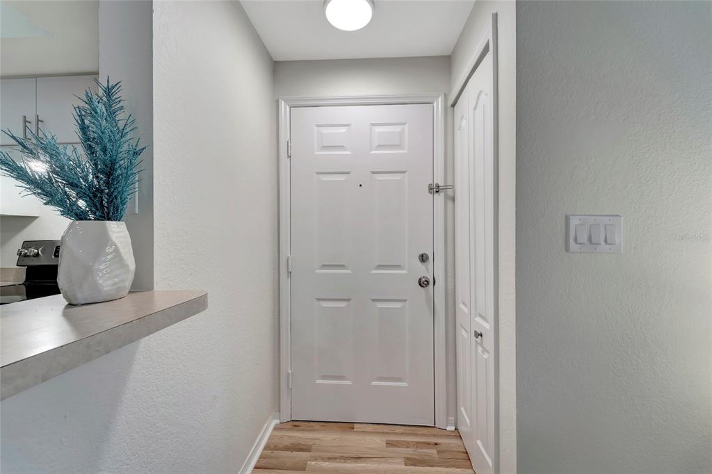 A white front door with a side closet stands in a small entryway with wood flooring — 4110 CENTRAL SARASOTA PARKWAY UNIT 125, SARASOTA, FL