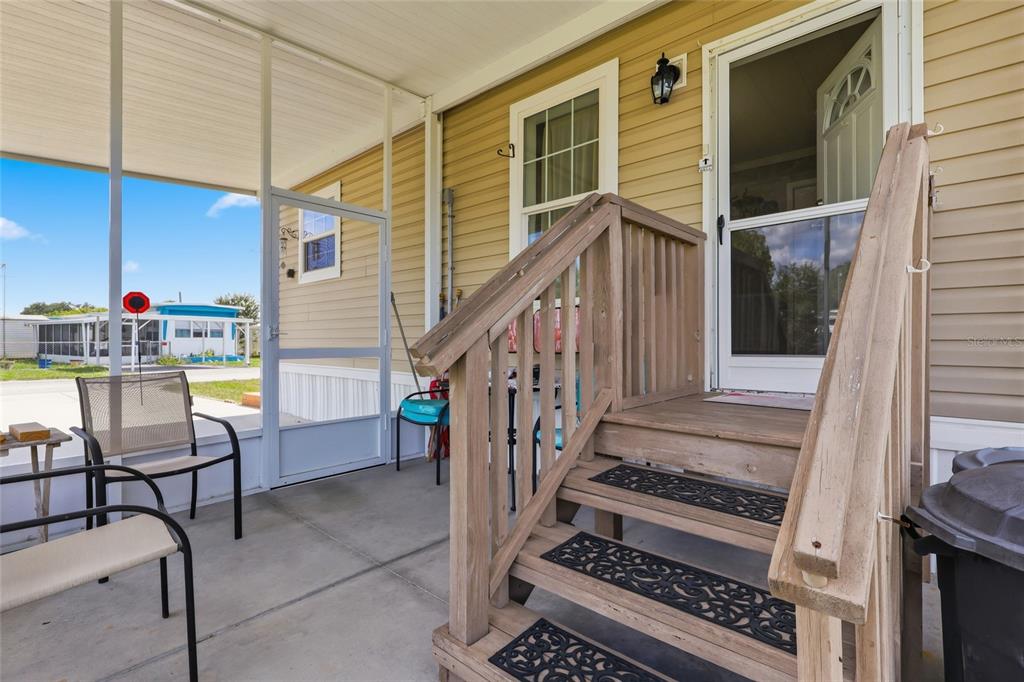 A screened-in porch features wooden stairs leading to a doorway with light yellow siding — 38745 NEW JERSEY AVENUE, ZEPHYRHILLS, FL