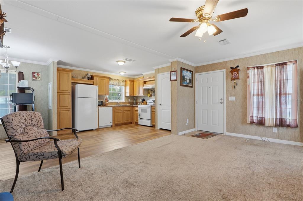 An open-concept living room with carpeted flooring transitions into a kitchen with wood cabinets — 38745 NEW JERSEY AVENUE, ZEPHYRHILLS, FL