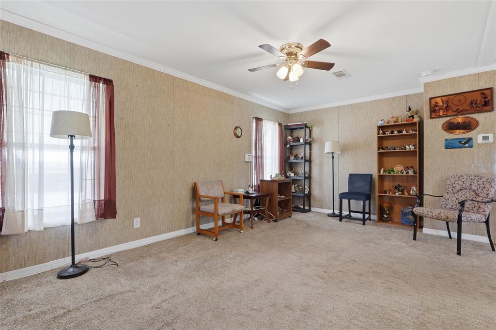A carpeted living room features beige textured walls, a ceiling fan, and various seating furniture — 38745 NEW JERSEY AVENUE, ZEPHYRHILLS, FL