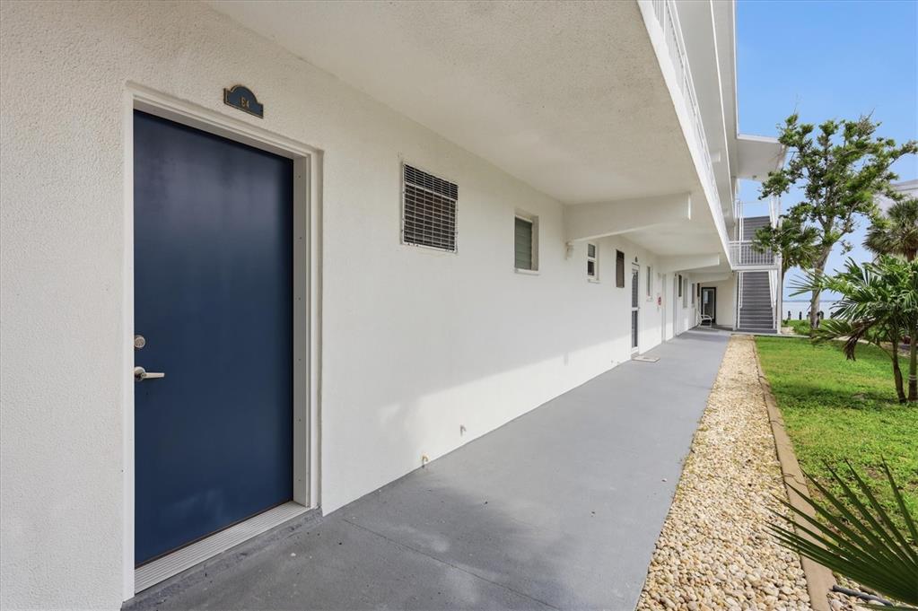 A blue door labeled E4 opens onto a concrete walkway beside a white building exterior — 769 JOHN RINGLING BOULEVARD UNIT 4, SARASOTA, FL