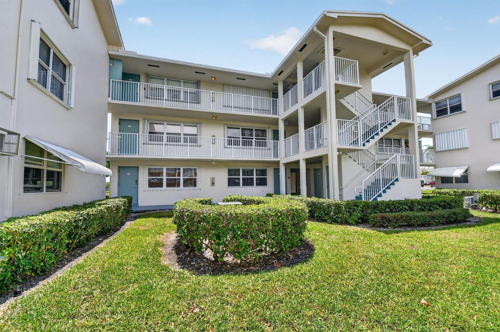 A three-story apartment building with exterior staircases, balconies, and manicured landscaping in the foreground — 370 Horizon Street E # 107, Boynton Beach FL 33435, BOYNTON BEACH, FL