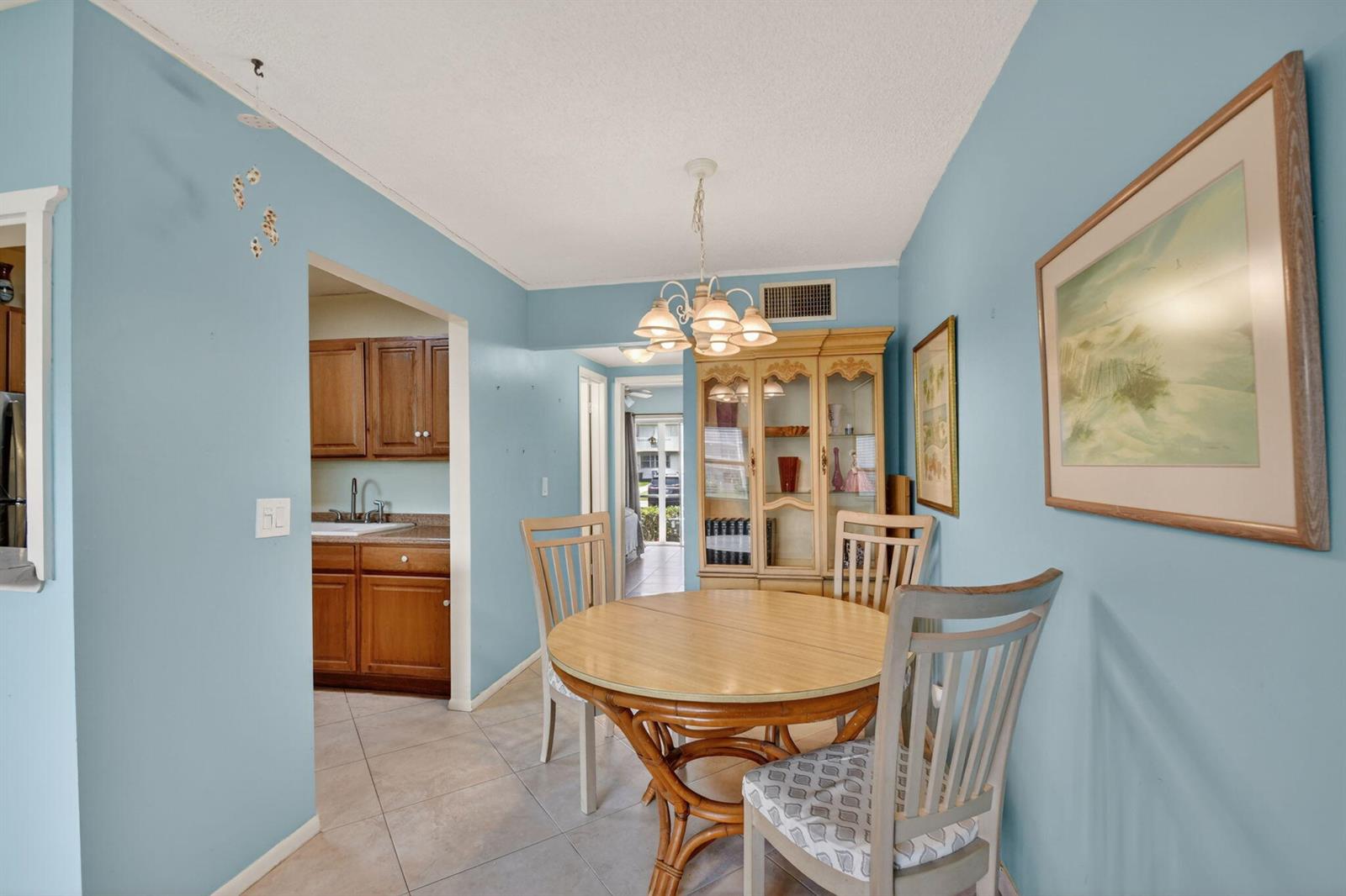 A dining area with a round wooden table, light blue walls, and a wooden hutch — 370 Horizon Street E # 107, Boynton Beach FL 33435, BOYNTON BEACH, FL