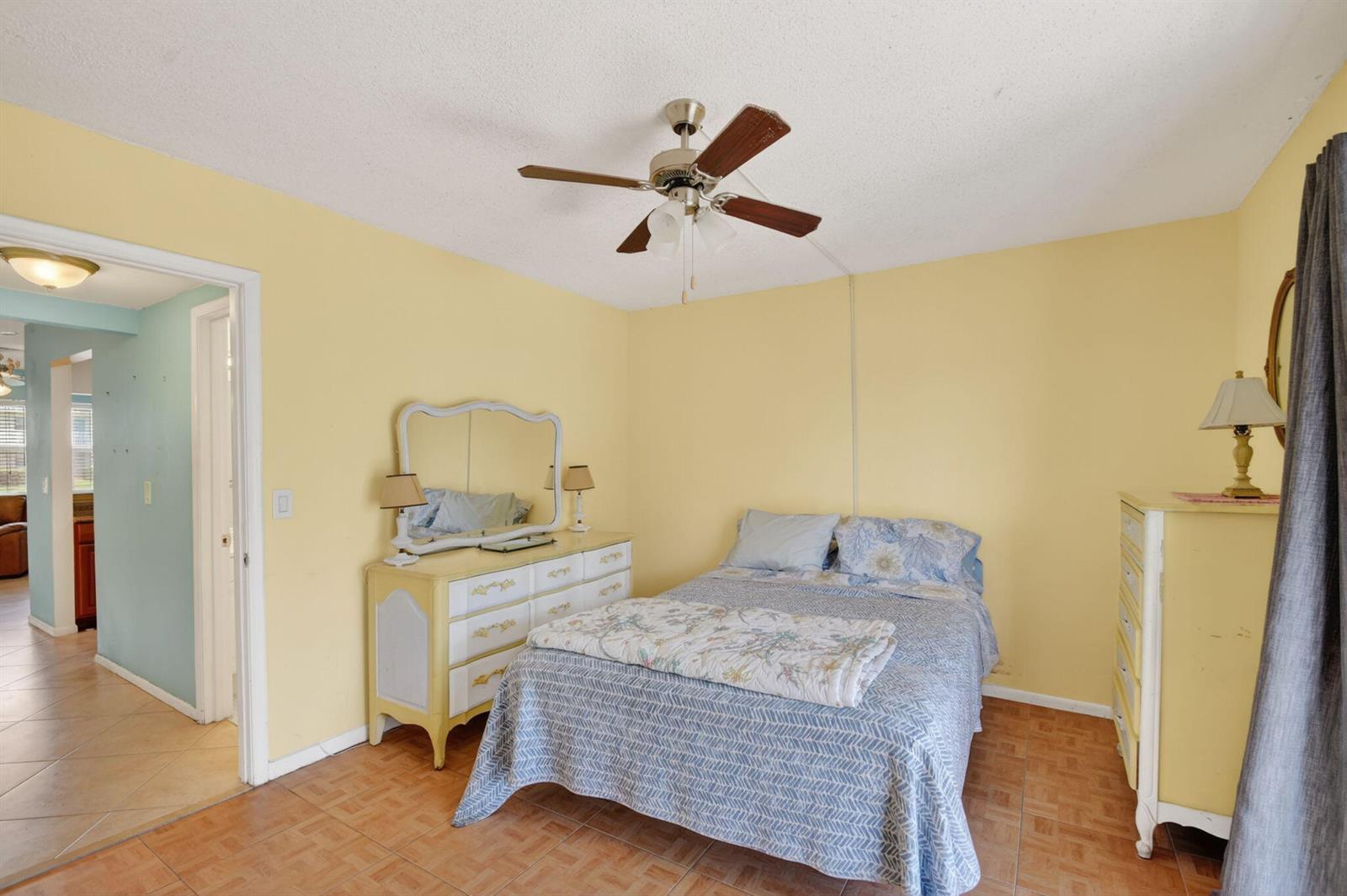 A bedroom with yellow walls, tile flooring, a ceiling fan, and light-colored wooden furniture — 370 Horizon Street E # 107, Boynton Beach FL 33435, BOYNTON BEACH, FL