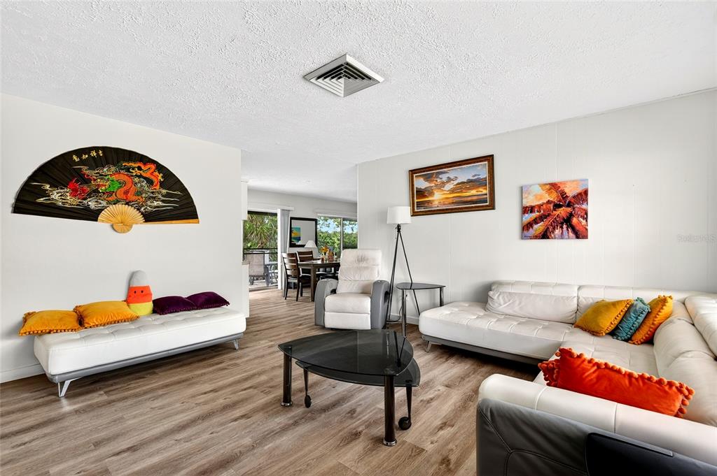 A living room features white leather sofas, wood-look flooring, and a decorative wall fan — 1565 S EVERGREEN AVENUE, CLEARWATER, FL