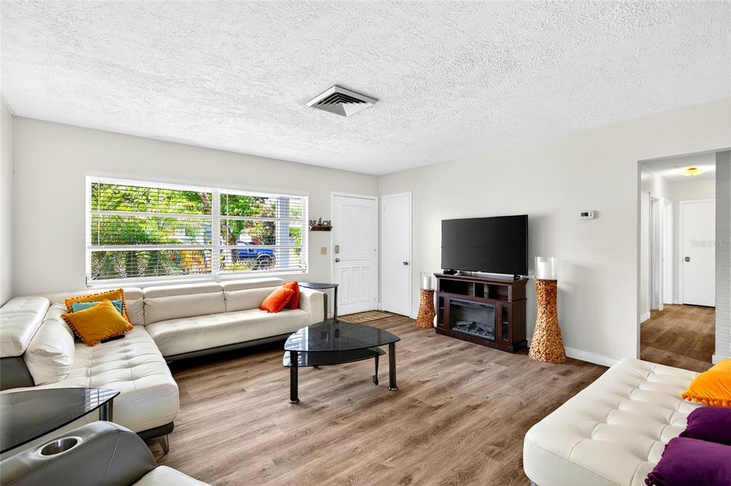 A living room features white sofas, a television on a media console, and wood-look flooring — 1565 S EVERGREEN AVENUE, CLEARWATER, FL