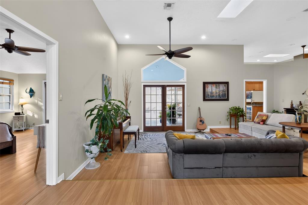 A living room with wood-look flooring, a gray sofa, a piano, and French doors — 4424 FRIAR TUCK LANE, SARASOTA, FL