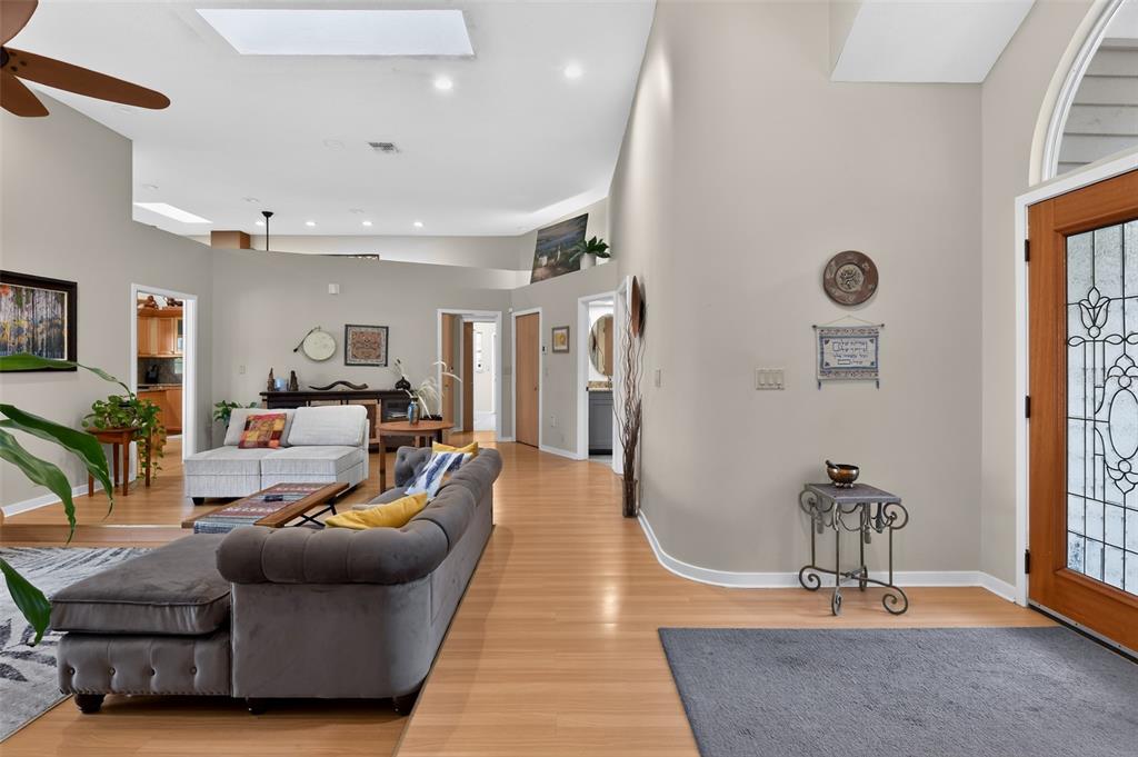 A living room with light wood flooring, a grey tufted sofa, and a front entryway — 4424 FRIAR TUCK LANE, SARASOTA, FL