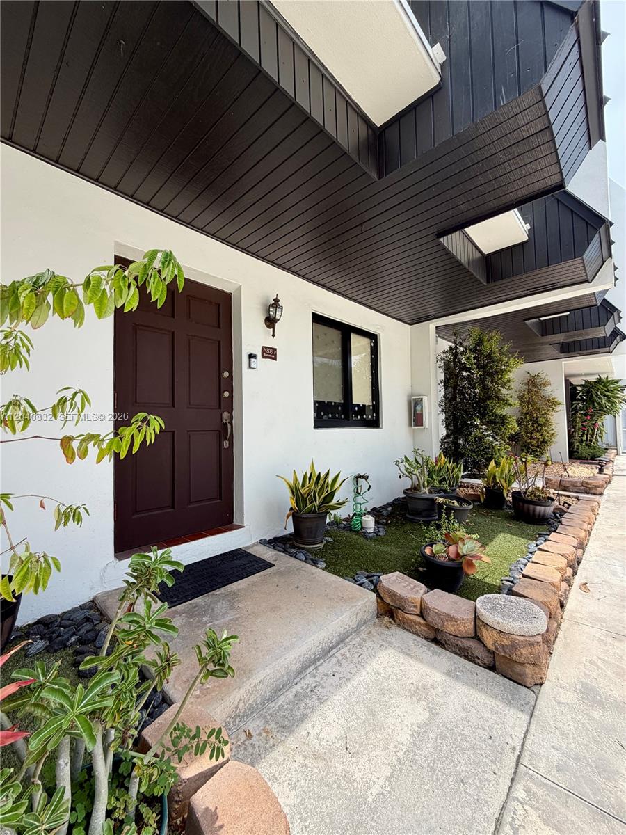 A brown front door sits beside a window and a small garden bed with potted plants — 6667 Miller Dr # 15, South Miami FL 33155, SOUTH MIAMI, FL