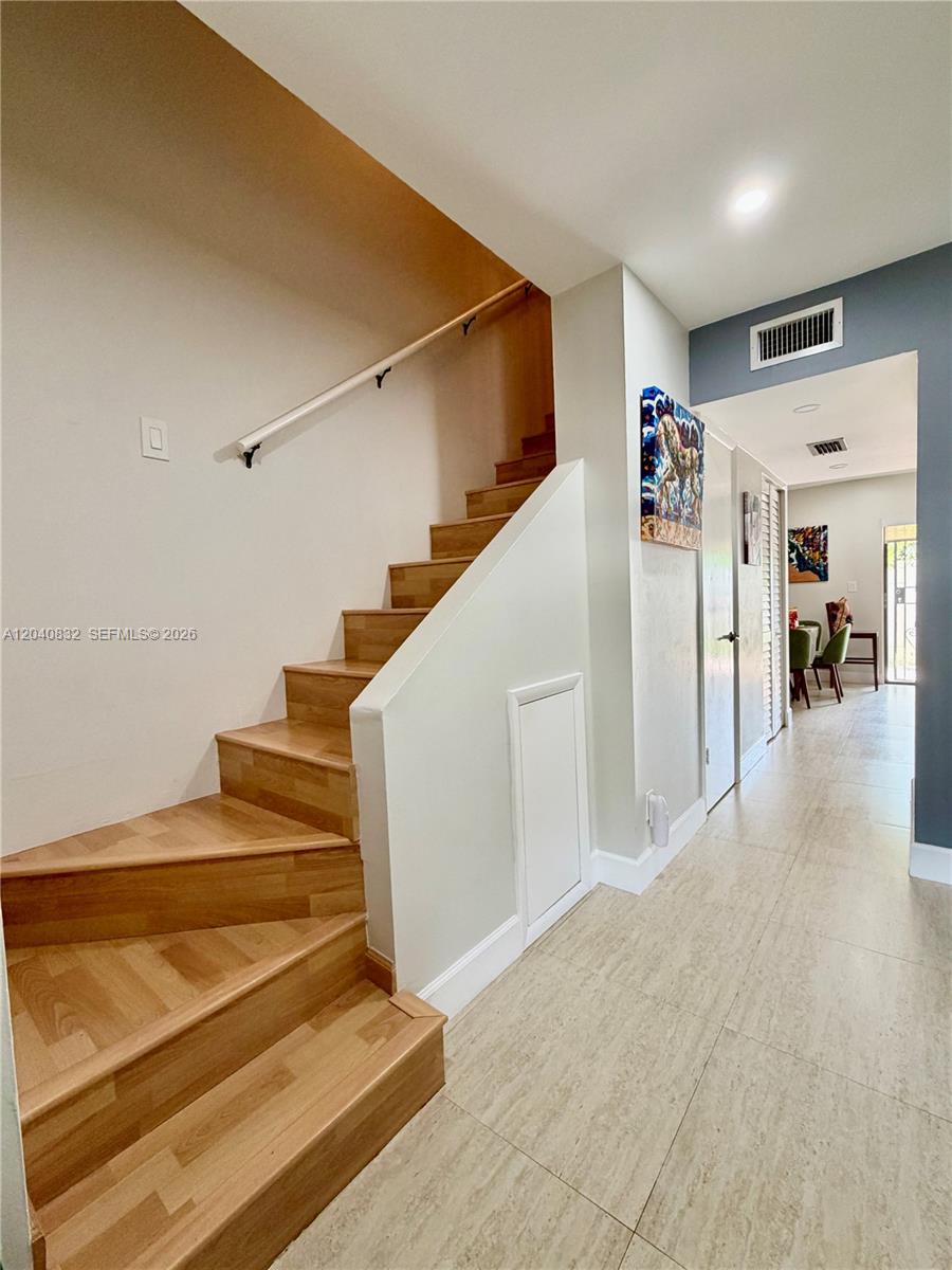 A wooden staircase with a white handrail leads upward next to a tiled hallway — 6667 Miller Dr # 15, South Miami FL 33155, SOUTH MIAMI, FL
