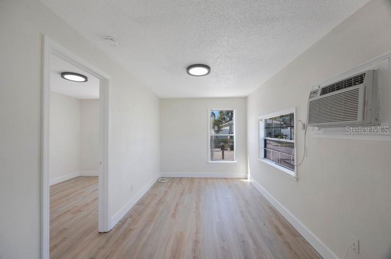 An empty room with light wood-look flooring, white walls, a window, and a wall-mounted air conditioner — 2753 53RD AVENUE N, ST PETERSBURG, FL