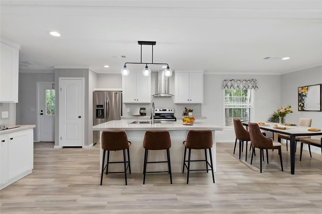 A modern kitchen features white cabinetry, a central island with bar seating, and dining area — 781 BAYOU DRIVE, CASSELBERRY, FL