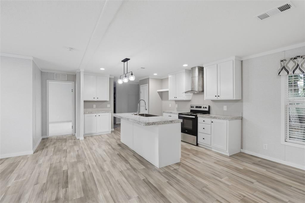 A kitchen with white cabinets, a central island, stainless steel appliances, and light wood flooring — 781 BAYOU DRIVE, CASSELBERRY, FL