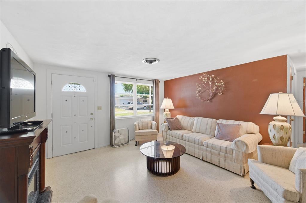 A living room features a striped sofa, a round coffee table, and a rust-colored wall — 3904 REDWOOD DRIVE, HOLIDAY, FL