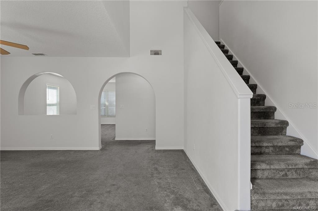 A living area with gray carpet, an arched wall cutout, and a carpeted staircase — 4482 E AVOCET COURT, INVERNESS, FL