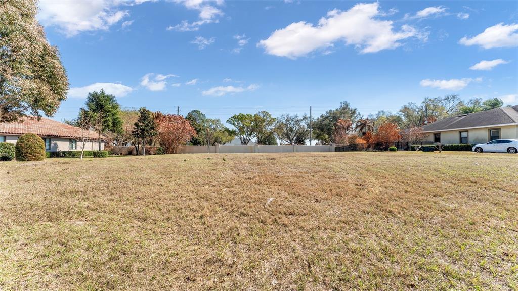 A wide, grassy vacant lot sits between two residential houses under a blue sky — 4410 EMERALD PALMS LANE, WINTER HAVEN, FL