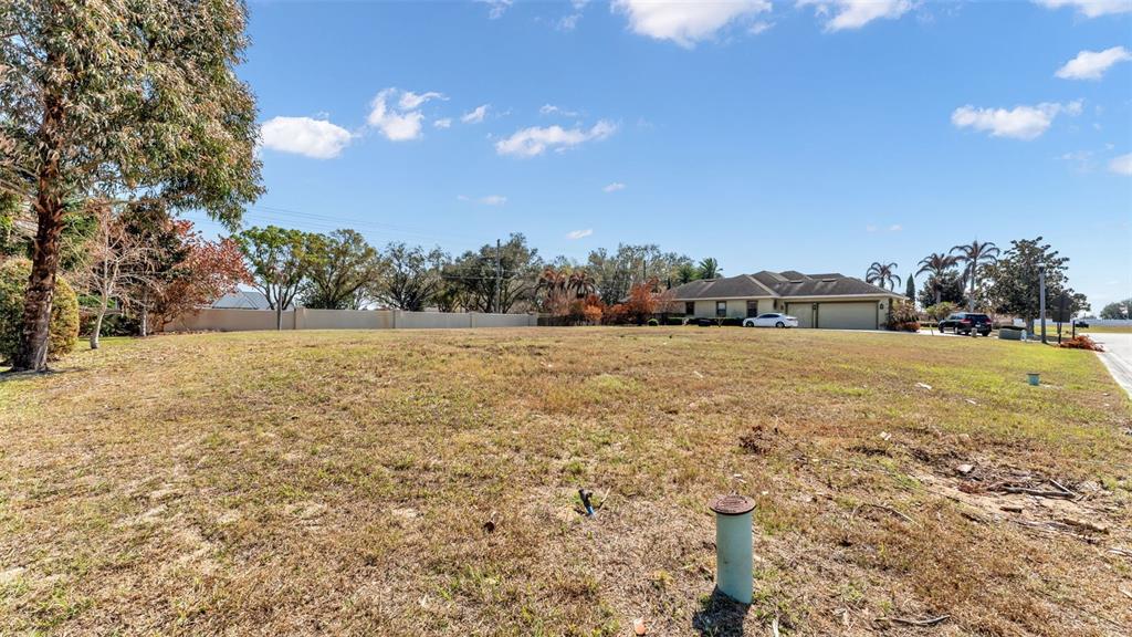A wide, grassy vacant lot with a house and trees in the background — 4410 EMERALD PALMS LANE, WINTER HAVEN, FL