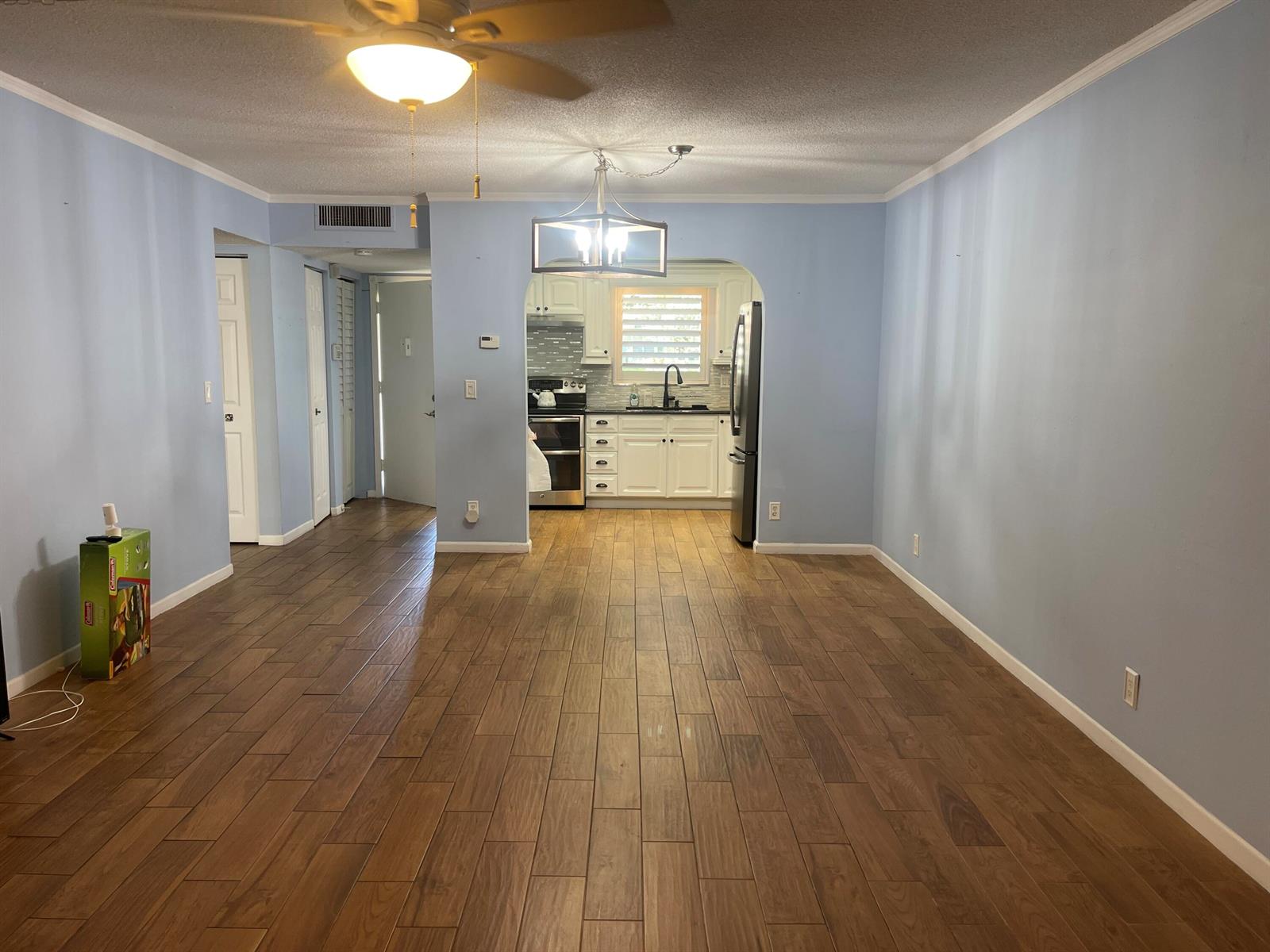 A living room with light blue walls and wood-look tile flooring leads to a kitchen — 752 Lori Drive # 223, Palm Springs FL 33461, PALM SPRINGS, FL