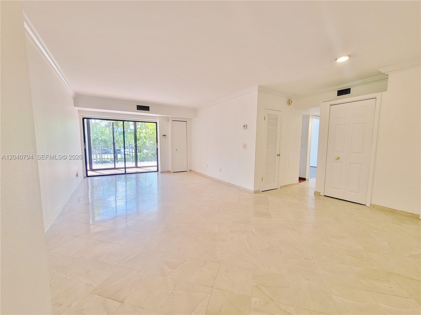 An empty room features white walls, beige tile flooring, and sliding glass doors to a balcony — 77 Crandon Blvd # 2B, Key Biscayne FL 33149, KEY BISCAYNE, FL