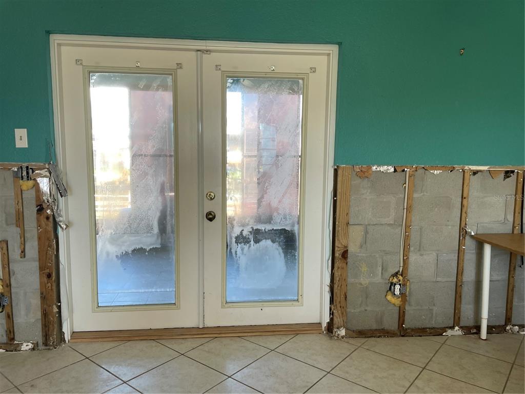A room with double glass doors, tile flooring, and unfinished walls exposing concrete blocks — 13612 FRANCES AVENUE, HUDSON, FL