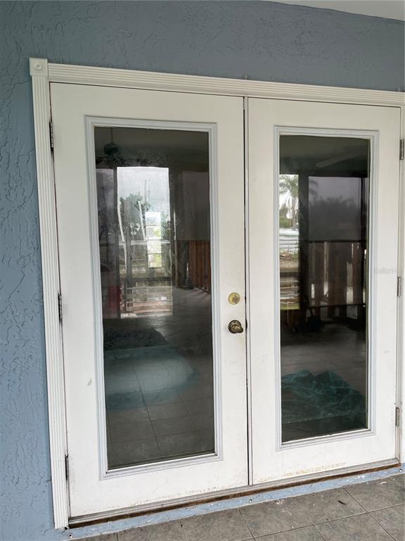 A set of white double glass doors with a brass handle on a blue exterior wall — 13612 FRANCES AVENUE, HUDSON, FL