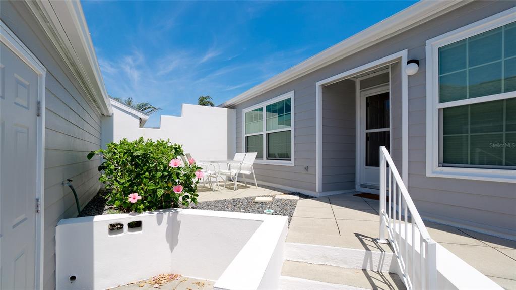 A patio area features a white wall, a small garden, and a concrete walkway — 1011 IBIS COURT, BRADENTON, FL