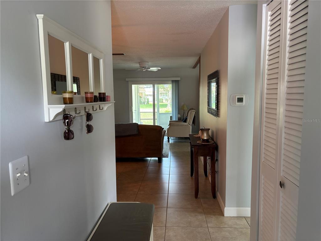 A hallway with tile flooring leads toward a living room with a sliding glass door — 668 PARK CIRCLE, BRADENTON, FL