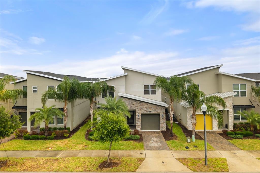 A row of modern townhouses with stone accents, palm trees, and paved driveways under a sky — 621 DROP SHOT DRIVE, DAVENPORT, FL