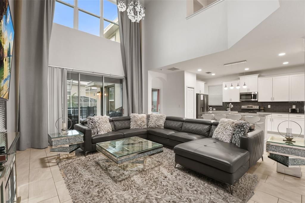 A spacious living room with high ceilings, a large sectional sofa, and an open kitchen — 621 DROP SHOT DRIVE, DAVENPORT, FL