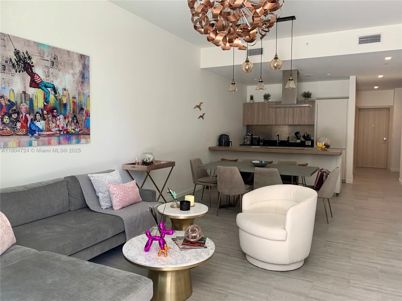 This open-concept living and dining area features a gray sectional, marble coffee tables, and modern lighting — 1000 Brickell Plz # 1805, Miami FL 33131, MIAMI, FL
