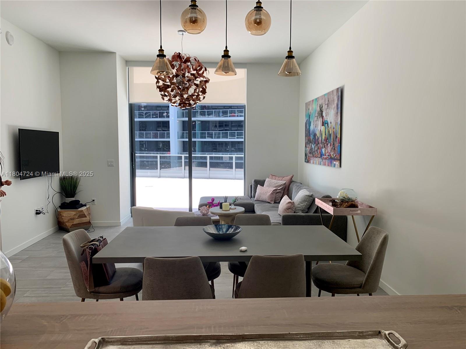 A modern dining and living area features a gray table, sectional sofa, and pendant lighting — 1000 Brickell Plz # 1805, Miami FL 33131, MIAMI, FL