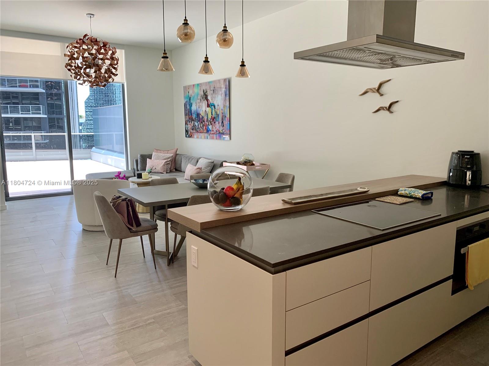 A modern kitchen island with a dark countertop sits before a dining area and balcony — 1000 Brickell Plz # 1805, Miami FL 33131, MIAMI, FL