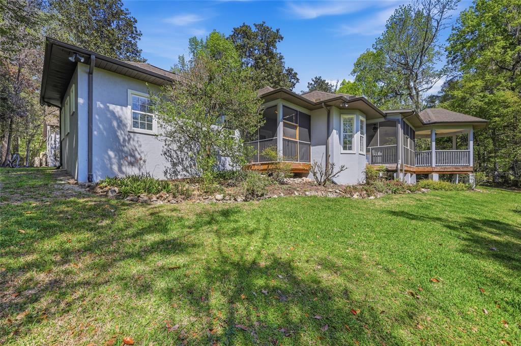 The exterior of a light-colored house features a screened-in porch and a wooden deck — 9510 NW 59TH LANE, GAINESVILLE, FL