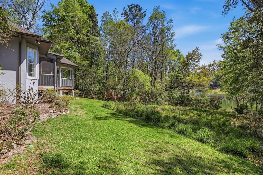 A grassy backyard leads to a wooded area and a pond next to a house — 9510 NW 59TH LANE, GAINESVILLE, FL