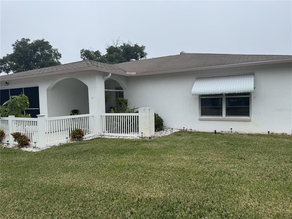 A white single-story house features a covered front porch, a white fence, and a window awning — 11220 ELDERBERRY DRIVE, PORT RICHEY, FL