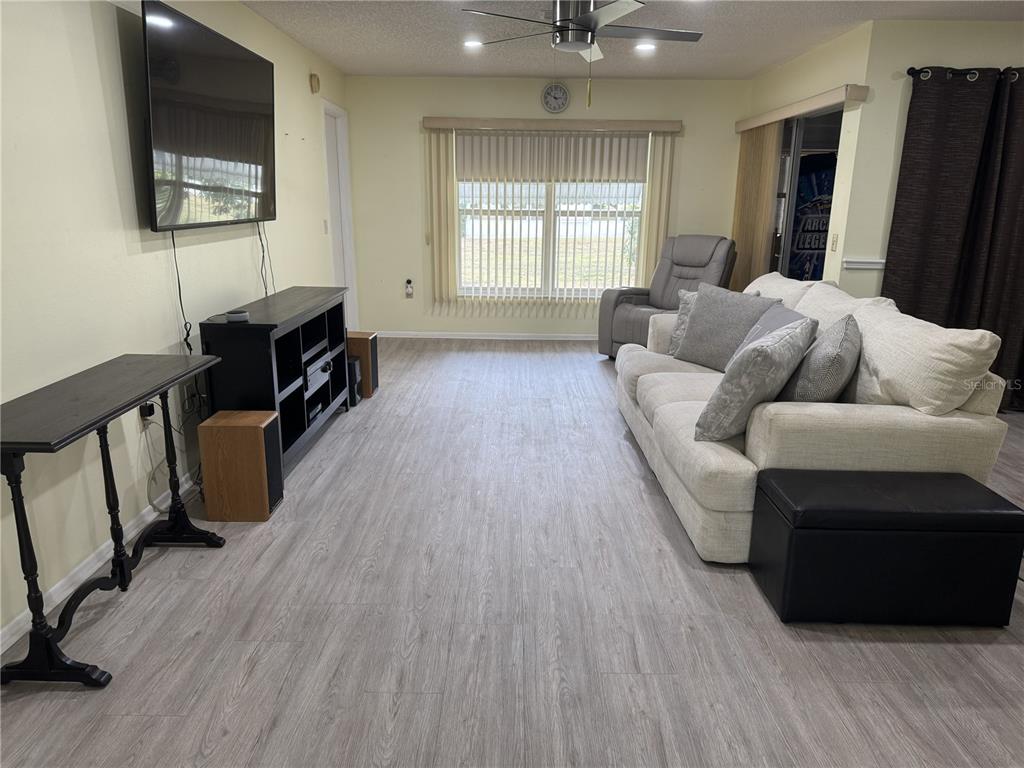 A living room features light wood-look flooring, a white sofa, and a wall-mounted television — 11220 ELDERBERRY DRIVE, PORT RICHEY, FL
