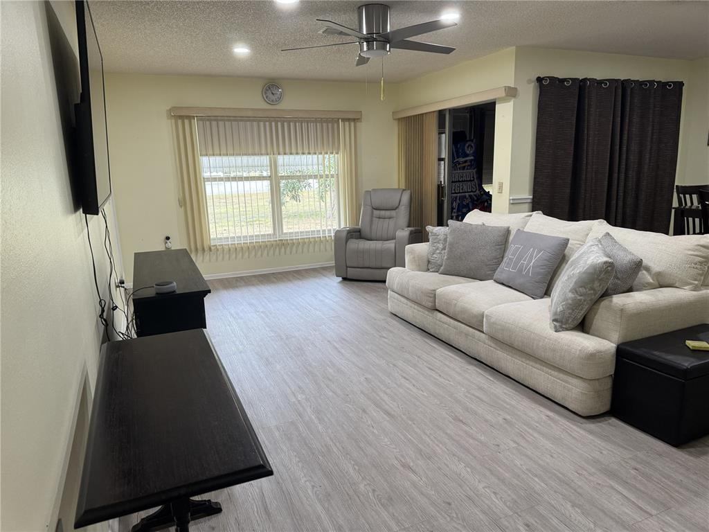 A living room features light wood-look flooring, a beige sofa, a recliner, and a ceiling fan — 11220 ELDERBERRY DRIVE, PORT RICHEY, FL