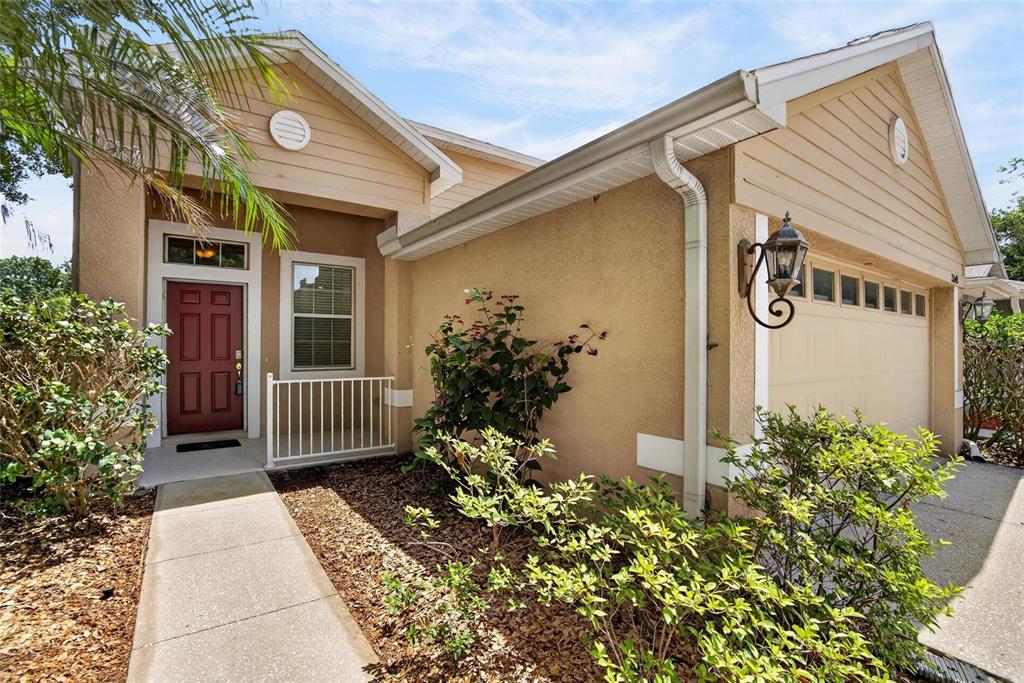 The exterior of a tan house features a red front door and a garage — 21040 GREEN WING COURT, LAND O LAKES, FL