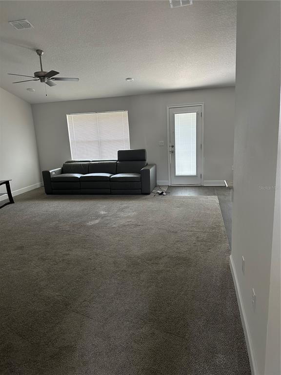 A living room features gray carpet, a dark leather sofa, a ceiling fan, and a door — 14 PRIMROSE LANE, PALM COAST, FL