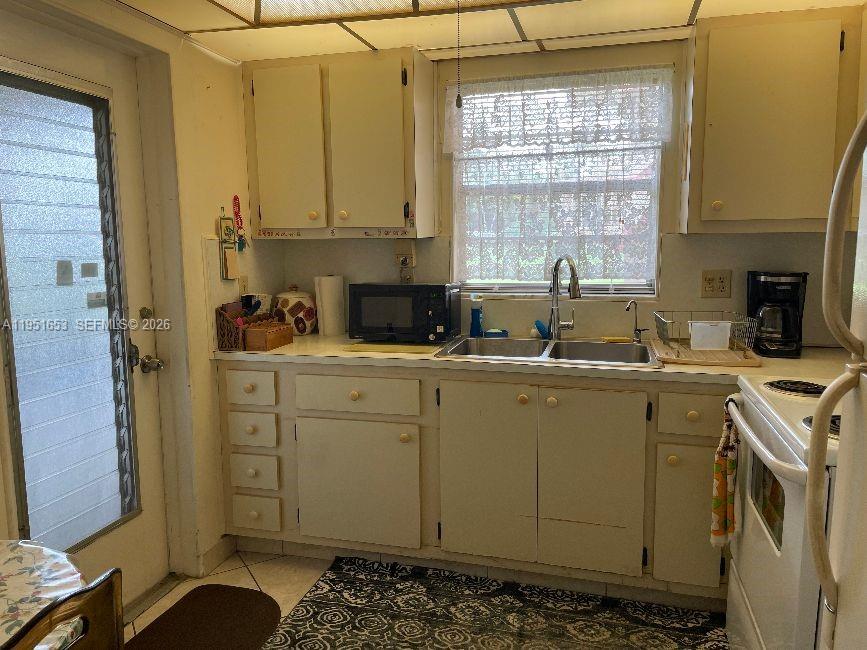 A kitchen features white cabinets, a double sink, a microwave, and a glass-paneled door — 5300 Washington St # S111, Hollywood FL 33021, HOLLYWOOD, FL