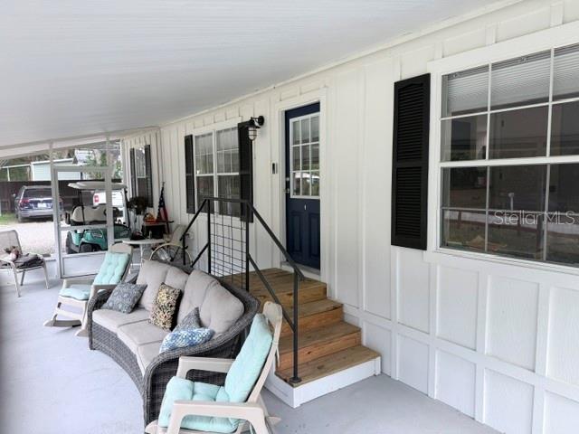 A covered porch features a wicker sofa, rocking chairs, a dark blue door, and wooden steps — 23065 SW 119TH PLACE, DUNNELLON, FL