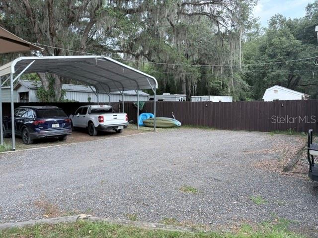 A gravel driveway features a metal carport sheltering a dark SUV and a white pickup truck — 23065 SW 119TH PLACE, DUNNELLON, FL